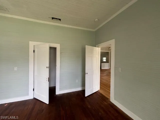 Unfurnished bedroom with crown molding and dark wood-style flooring