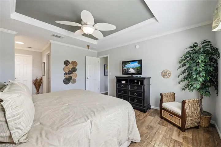 Bedroom featuring ornamental molding, light wood-style flooring, a ceiling fan, and a raised ceiling