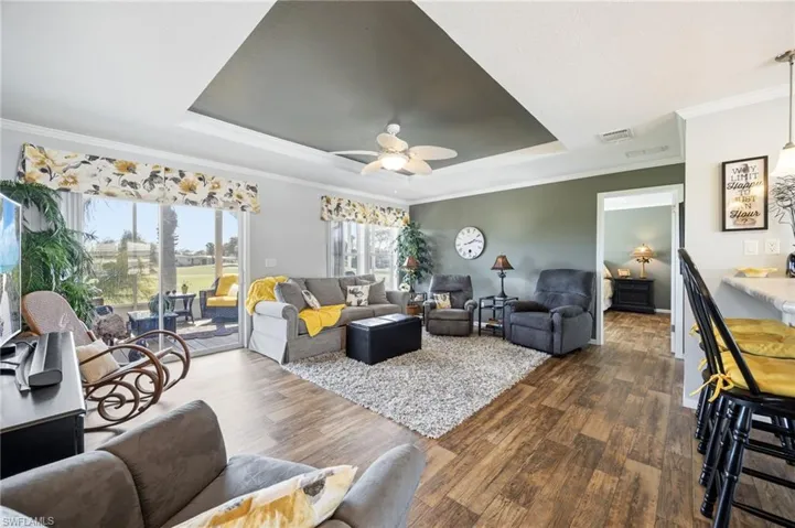 Living room with crown molding, a ceiling fan, dark wood-type flooring, and a tray ceiling