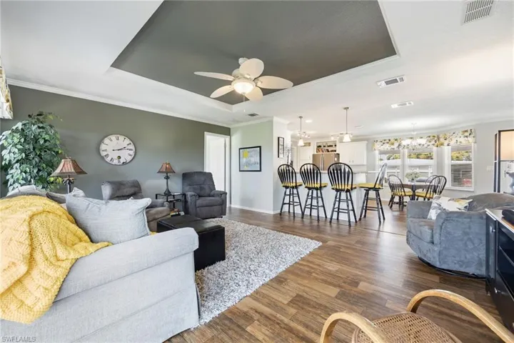 Living room featuring ceiling fan, a tray ceiling, dark wood-style flooring, ornamental molding, and hanging lights