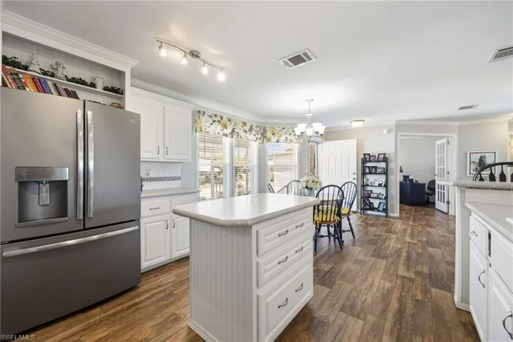 Kitchen with ornamental molding, stainless steel refrigerator with ice dispenser, white cabinets, light countertops, and dark wood finished floors