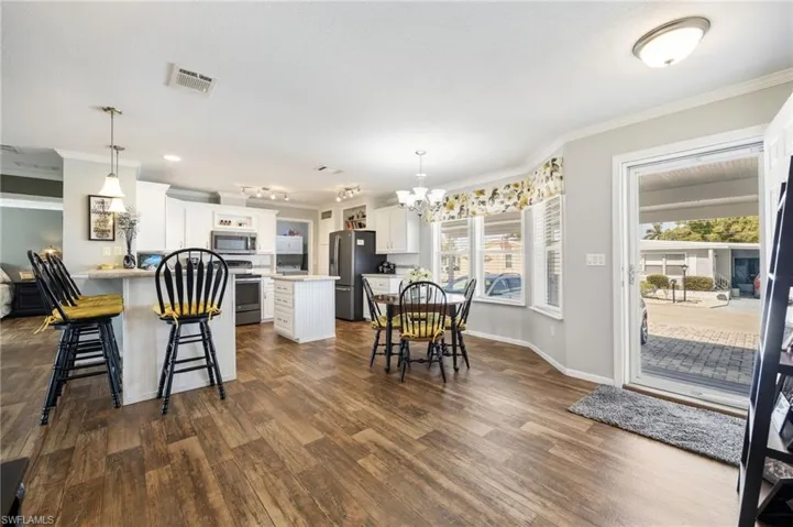 Kitchen featuring ornamental molding, a breakfast bar area, a chandelier, white cabinetry, and stainless steel appliances