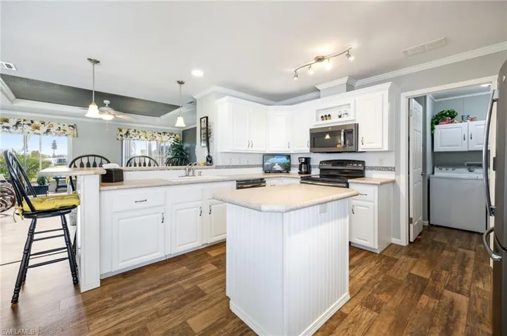 Kitchen featuring ornamental molding, a peninsula, a breakfast bar area, white cabinets, and decorative light fixtures