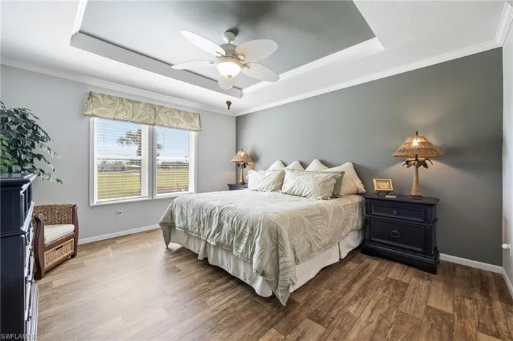 Bedroom featuring crown molding, dark wood finished floors, a ceiling fan, and a tray ceiling