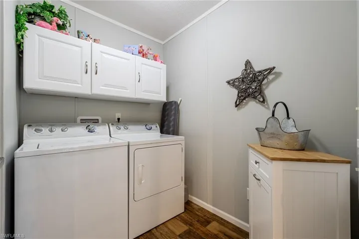 Laundry area featuring cabinet space, separate washer and dryer, dark wood-style flooring, ornamental molding, and a textured ceiling
