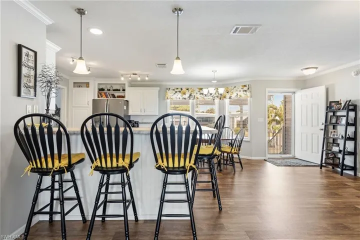Kitchen with ornamental molding, freestanding refrigerator, white cabinetry, a kitchen breakfast bar, and dark wood-style flooring