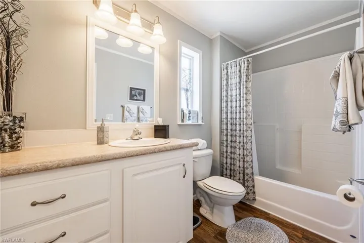 Full bathroom with vanity, shower / bath combination with curtain, ornamental molding, and dark wood-style floors