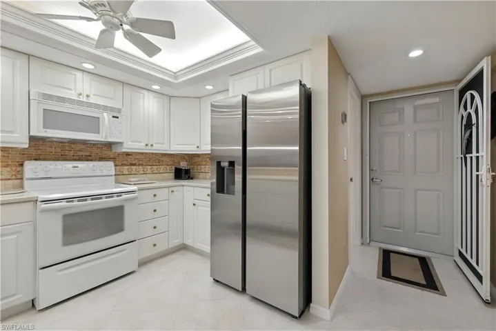Kitchen featuring white appliances, recessed lighting, light countertops, white cabinets, and decorative backsplash