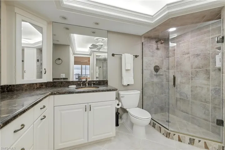 Bathroom featuring a shower stall, vanity, light tile patterned floors, ceiling fan, and ornamental molding