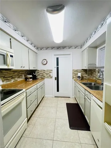 Kitchen featuring white appliances, decorative backsplash, light countertops, white cabinets, and light tile patterned floors