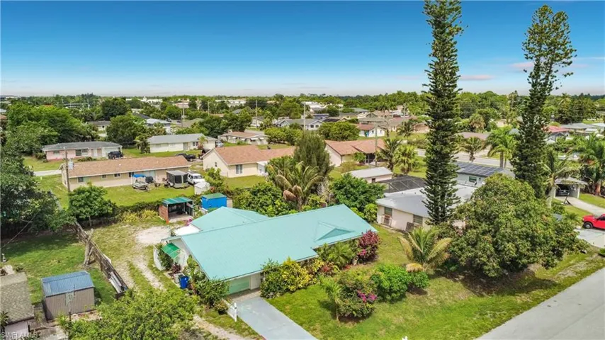 Single-story residence featuring a light blue metal roof, an attached garage, a paved driveway, mature landscaping, and a fenced yard