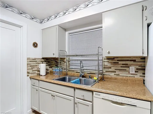 Kitchen area featuring light-toned cabinetry, a stainless steel double basin sink, and a multi-toned tile backsplash