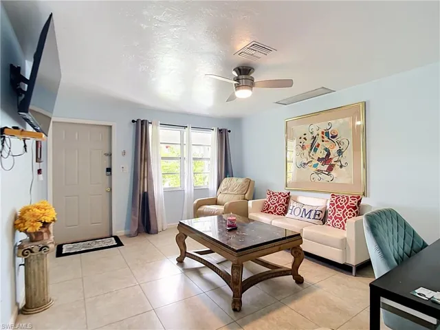 Light-colored tile flooring throughout a bright living space featuring a ceiling fan, a window with horizontal panes, and a paneled entry door
