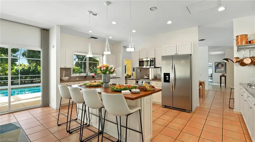 Kitchen with appliances with stainless steel finishes, a kitchen bar, hanging light fixtures, a kitchen island, and white cabinetry