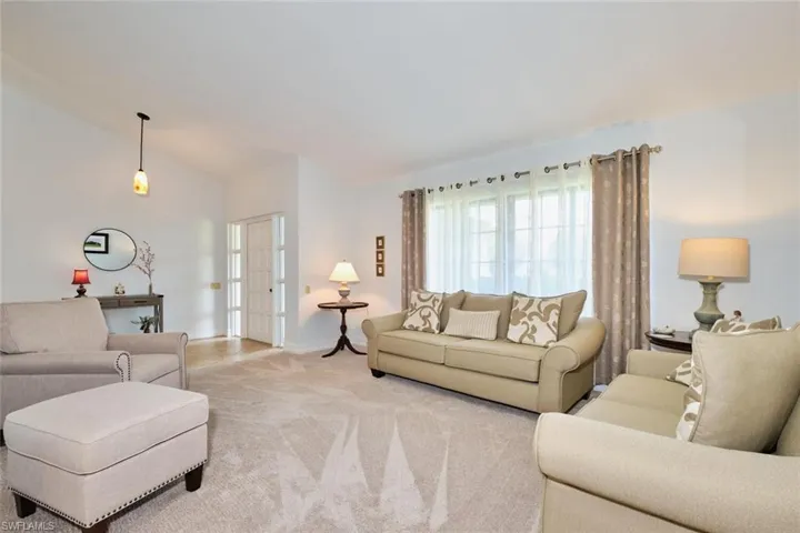 Spacious living room with light colored carpet, and vaulted ceiling.