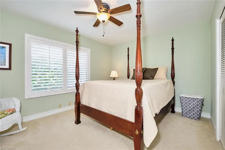 Guest bedroom with plantation shutters,  carpet floors, and a lighted ceiling fan