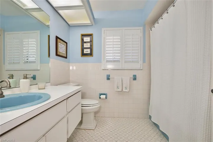 Full bath with tile patterned flooring, tile walls, tub and shower combo, plantation shutters.