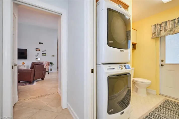 Utility room with light tile patterned floors, stacked washer and clothes dryer, and a half bath with pool access.