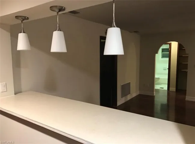 Kitchen featuring arched walkways, dark wood finished floors, hanging light fixtures, and light countertops
