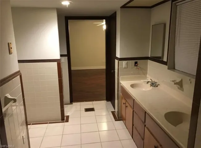 Bathroom featuring double vanity, light tile patterned floors, tile walls, a ceiling fan, and wainscoting