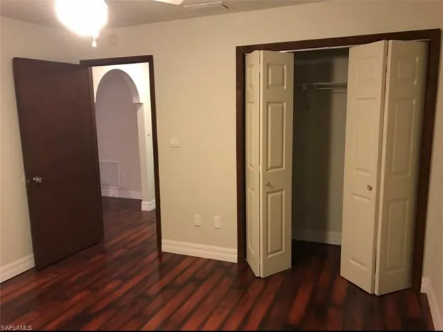 Unfurnished bedroom featuring dark wood finished floors, a ceiling fan, a closet, and arched walkways