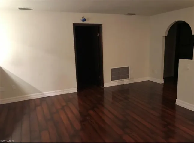 Empty room featuring arched walkways and dark wood-style floors