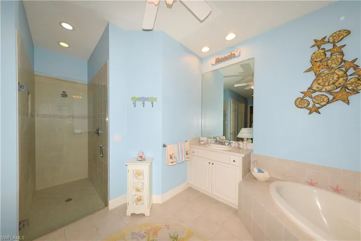 Spa-like en-suite bath features dual Corian vanities with large mirrors, soaking tub, walk-in shower with frameless glass, upgraded tile, and shampoo niche, recessed lighting, linen closet, and a private water closet.