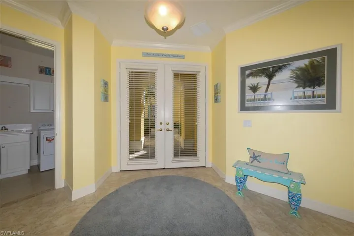 Entry foyer with French  door entryway. Laundry room to left  and guest bedroom and bath to right. Features 20" diagonal tile flooring, 10' ceilings, 8' doorways & Crown molding.