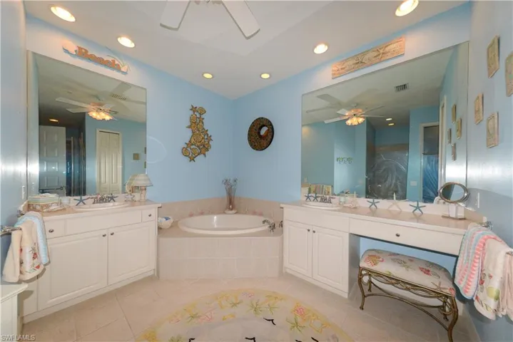 Spa-like en-suite bath features dual Corian vanities with large mirrors, soaking tub, walk-in shower with frameless glass, upgraded tile, and shampoo niche, recessed lighting, linen closet, and a private water closet.