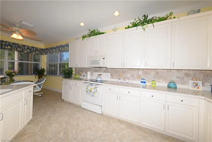 Spacious Kitchen with white cabinetry, 42" upper cabinets, Corian counters, Tile backsplash, Crown Molding and a pantry.