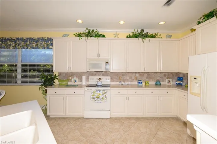 Spacious Kitchen with white cabinetry, 42" upper cabinets, soft close drawers, Corian counters, tile backsplash, Crown Molding and a pantry.