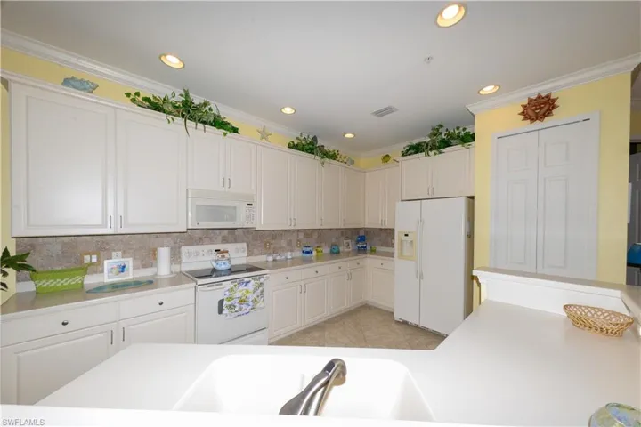 Spacious Kitchen with white cabinetry, 42" upper cabinets, Corian counters, Tile backsplash, Crown Molding and a pantry.