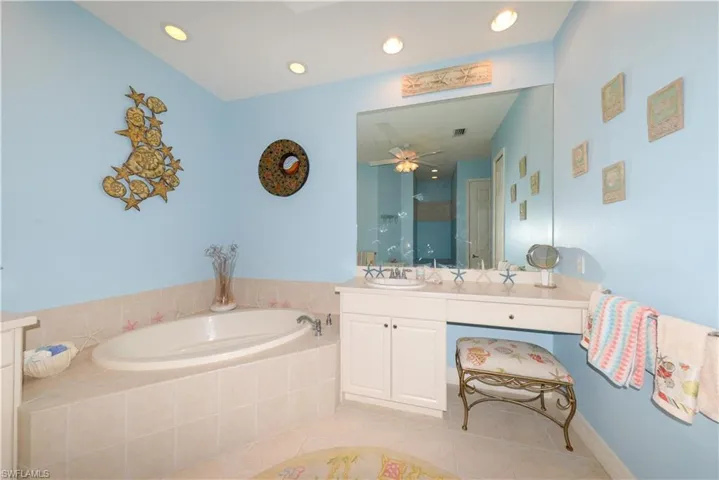 Spa-like en-suite bath features dual Corian vanities with large mirrors, soaking tub, walk-in shower with frameless glass, upgraded tile, and shampoo niche, recessed lighting, linen closet, and a private water closet.