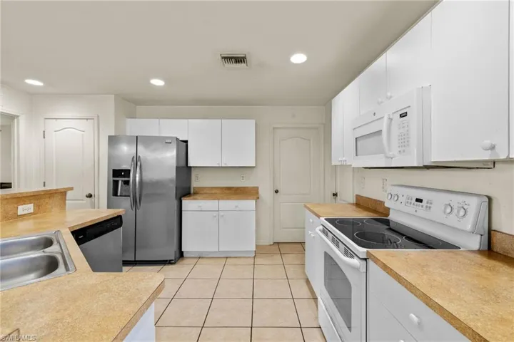 Kitchen featuring white appliances, recessed lighting, light countertops, white cabinets, and light tile patterned flooring