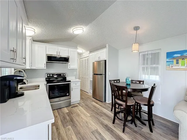Kitchen featuring appliances with stainless steel finishes, light wood-type flooring, pendant lighting, a textured ceiling, and white cabinets