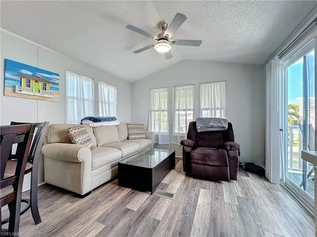 Living area featuring light wood finished floors, healthy amount of natural light, lofted ceiling, a textured ceiling, and ceiling fan