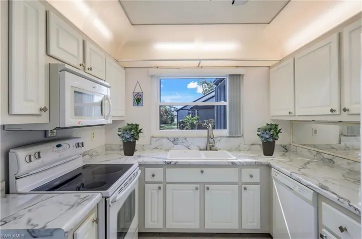 Kitchen featuring decorative backsplash, white cabinetry, white appliances, and sink