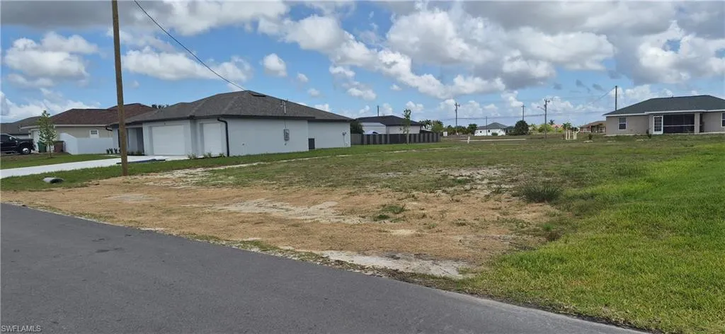 Spacious lot featuring grass and ground cover, with a paved road present in the foreground