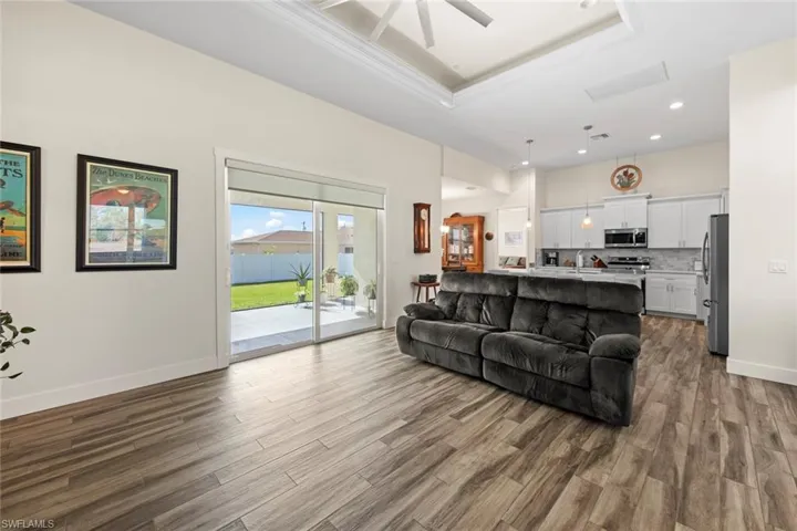 Living room with a tray ceiling, ceiling fan, crown molding, sink, and wood-type flooring