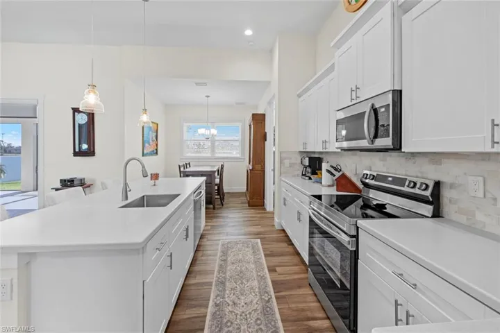 Kitchen with pendant lighting, a kitchen island with sink, sink, appliances with stainless steel finishes, and white cabinetry