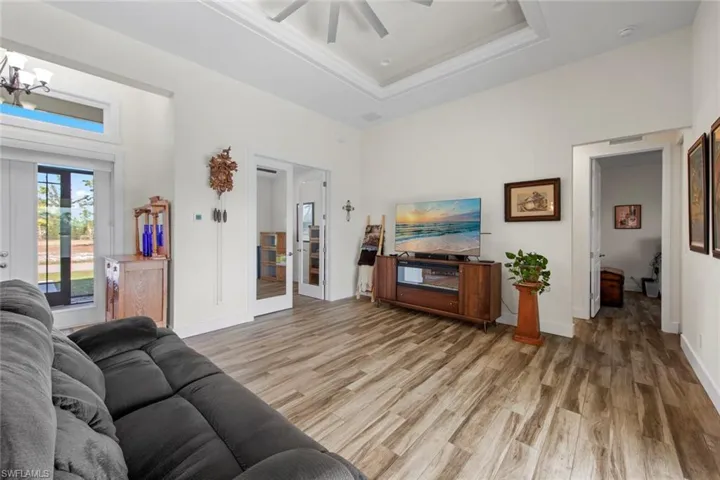 Living room with french doors, ceiling fan, a raised ceiling, ornamental molding, and wood-type flooring