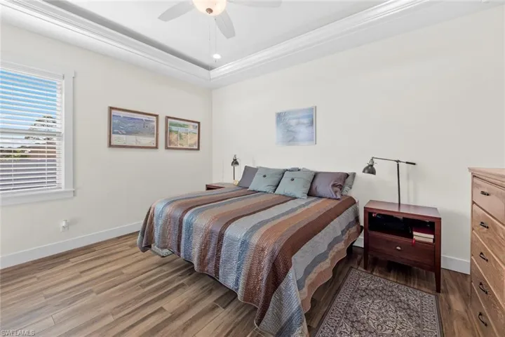 Bedroom with hardwood / wood-style floors, ceiling fan, a raised ceiling, and crown molding