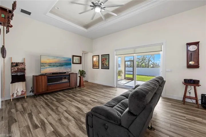 Living room with hardwood / wood-style floors, ceiling fan, a raised ceiling, and crown molding
