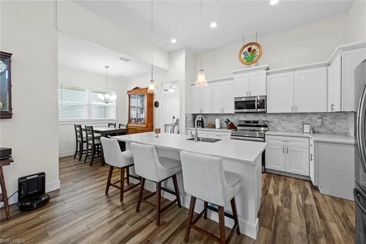 Kitchen with pendant lighting, a kitchen island with sink, white cabinets, sink, and appliances with stainless steel finishes