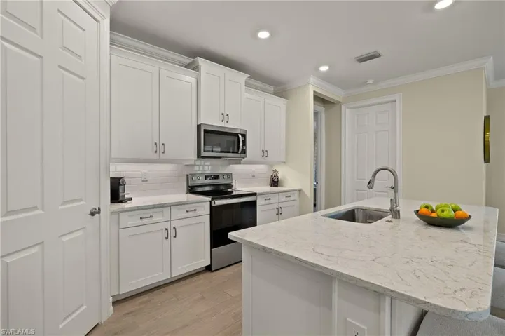 Kitchen with sink, white cabinetry, stainless steel appliances, light stone countertops, and a kitchen island with sink