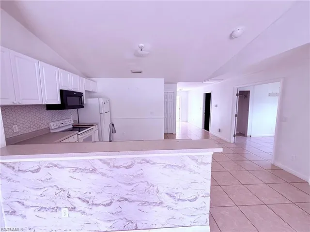Kitchen with lofted ceiling, light countertops, white range with electric cooktop, light tile patterned flooring, and white cabinetry