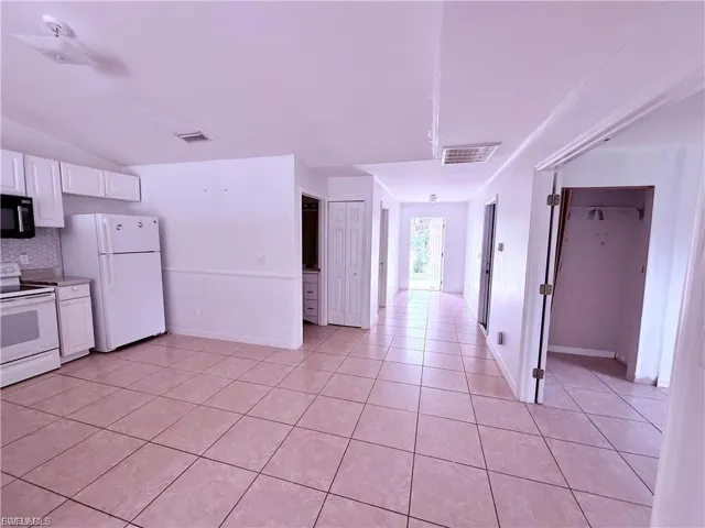 Kitchen featuring white appliances, white cabinetry, light countertops, light tile patterned floors, and vaulted ceiling