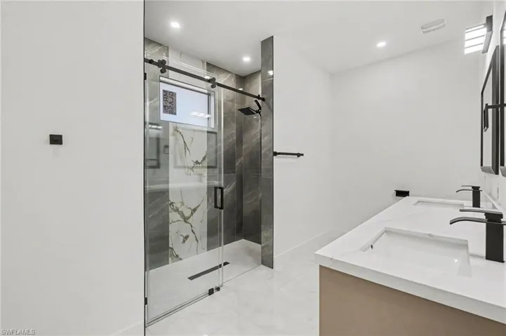 Primary bathroom with walk-in shower and modern finishesfinish shower, double vanity, and recessed lighting