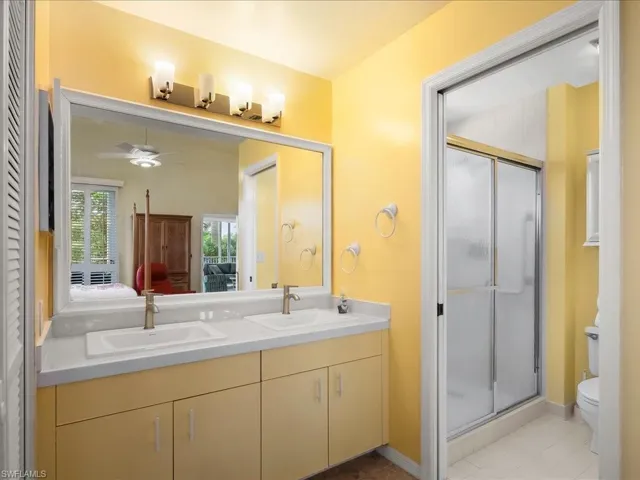 Ensuite bathroom with a shower stall, double vanity, ceiling fan, and light tile patterned floors
