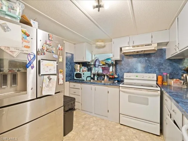 Kitchen with electric stove, stainless steel fridge with ice dispenser, sink, and white cabinets